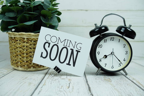 Скоро текст на бумажной карточке с будильником на деревянном фоне