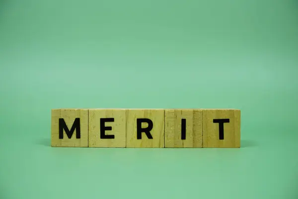 Stock image Merit with wooden blocks alphabet letters on green background