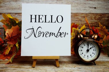 Merhaba Kasım ayının alarm saati ve ahşap zemin üzerinde akçaağaç yaprağı süslemesi olan metni