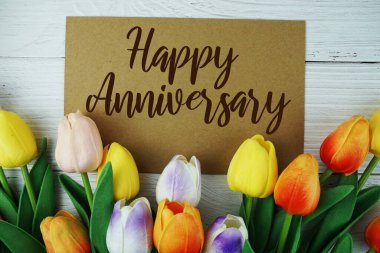 Ahşap arkaplanda çiçek çerçeveli Mutlu Yıldönümü tipografisi metni