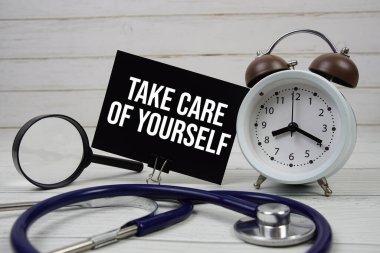 Kağıt üzerinde steteskop, çalar saat ve tahta arka planda büyüteçle kendine dikkat et.