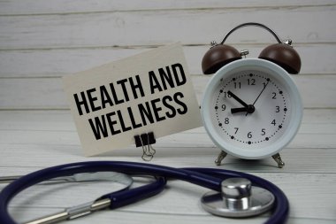 Kağıt üzerinde steteskoplu sağlık ve sağlık mesajı ve ahşap zemin üzerinde alarm saati.