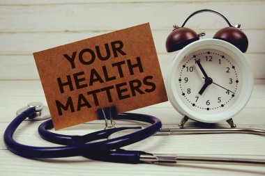 Sağlık Meseleleriniz kağıt karta steteskop ve ahşap zemin üzerindeki çalar saatle mesaj atıyor.