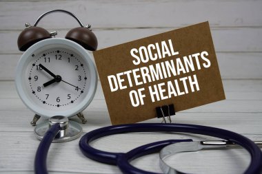 Social Determinants Of Health text message on paper card with stethoscope and alarm clock on wooden background clipart