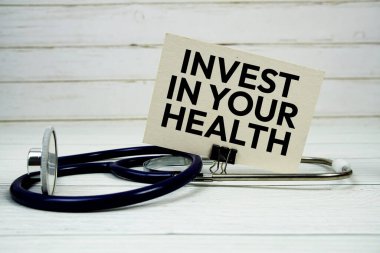 Tahta arka planda steteskop bulunan kağıt kartınıza sağlık mesajınıza yatırım yapın