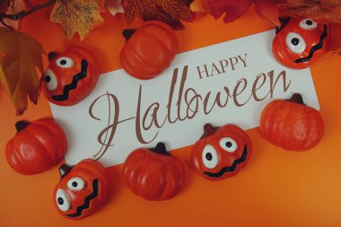 Turuncu arka planda balkabağı süslemesi olan kağıt üzerinde mutlu Cadılar Bayramı metinleri