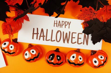 Turuncu arka planda balkabağı süslemesi olan kağıt üzerinde mutlu Cadılar Bayramı metinleri