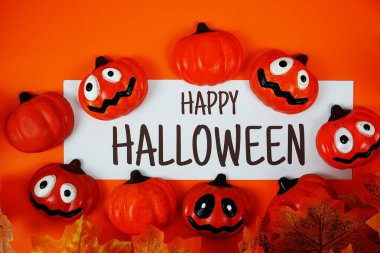 Turuncu arka planda balkabağı süslemesi olan kağıt üzerinde mutlu Cadılar Bayramı metinleri