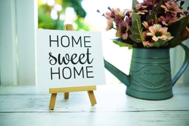 Home Sweet Home gazetesi, arka planında sehpa ve alarmlı saat olan kağıt kart üzerindeki metinden alıntılar yapıyor