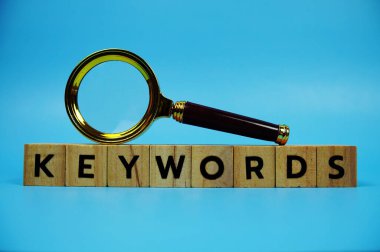 Ahşap blok alfabe harfleri ve mavi arkaplanda büyüteç içeren anahtar kelimeler