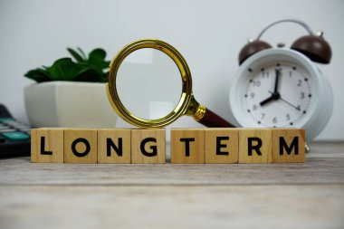 Tahta bloklar alfabe harfli büyüteç ve alarm saati. Ahşap arka planda uzun dönem mesajları.