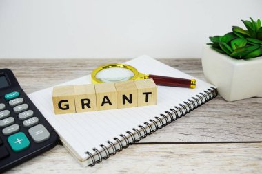 Tahta bloklar alfabe harfli büyüteç ve hesap makinesi ahşap zemin üzerinde GRANT metin mesajı