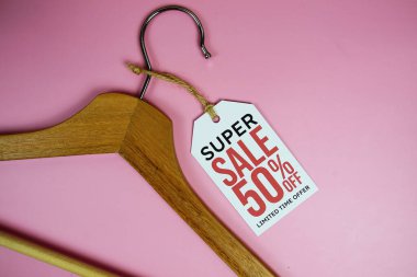 % 50 indirimli fiyat etiketi, ahşap elbise askısı pembe arka planda üst görünüm.
