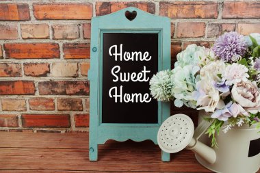 Home Sweet Home 'un karatahta sehpasında eski tuğla duvardaki vazoda çiçekler olan metni.