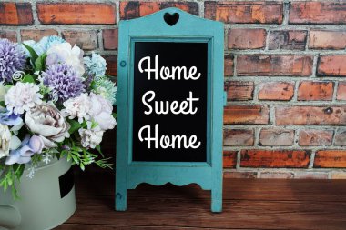 Home Sweet Home 'un karatahta sehpasında eski tuğla duvardaki vazoda çiçekler olan metni.