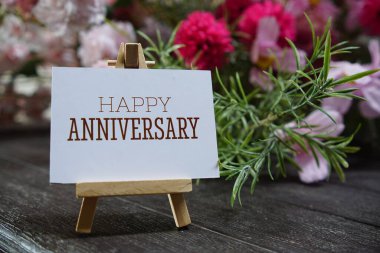 Kağıt kağıda tahta sehpa ve ahşap arka planda çiçek süslemesi yazılı mutlu yıldönümü metinleri