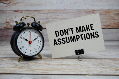 Tahta arka planda çalar saat olan kağıt üzerinde varsayımlar yazma