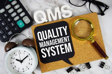 QMS - Hesap makinesi, alarm saati ve büyüteç ile Kalite Yönetim Sistemi kısaltması, iş konsepti arka planı