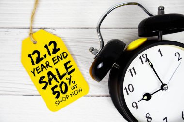 12.12 Yıl Sonu İndirimi% 50 indirimli fiyat etiketi ve ahşap arka planda alarm saati
