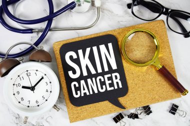 Cilt kanseri konuşma balonunda alarm saati, büyüteç ve mermer zemin üzerinde steteskop.