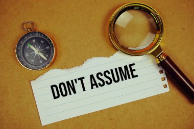 Don't Assume text on paper torn with compass and magnifying glass on paper craft background clipart