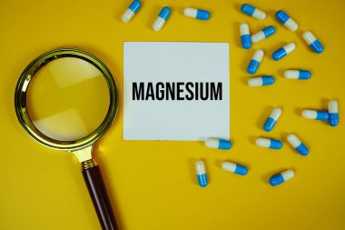 İlaç kapsülü ve sarı zemin üzerinde büyüteç bulunan yapışkan kağıt üzerinde magnezyum metin