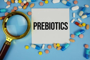 Mavi zemin üzerinde ilaç ve büyüteç bulunan yapışkan not kağıdı üzerindeki prebiyotik metni