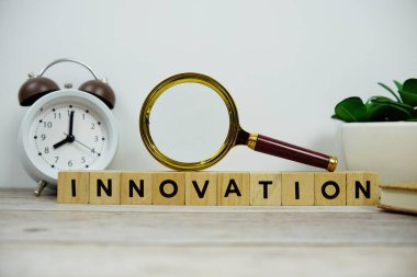 Tahta bloklar alfabe harfleriyle büyüteç ve alarm saati Ahşap zemin üzerinde Innovation metin