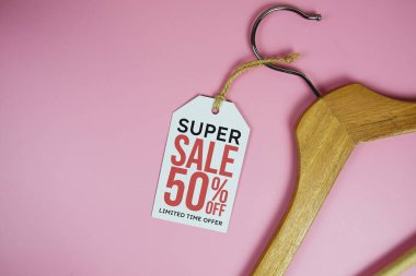 % 50 indirimli fiyat etiketi, ahşap elbise askısı pembe arka planda üst görünüm.