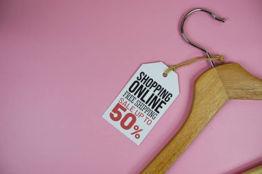 İnternetten alışveriş% 50 'ye varan fiyat etiketi, ahşap elbise askısı, pembe arka planda üst görünüm.