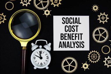 SCBA - Social Cost Benefit Analysis text message on sticky note with magnifying glass and alarm clock on black background clipart