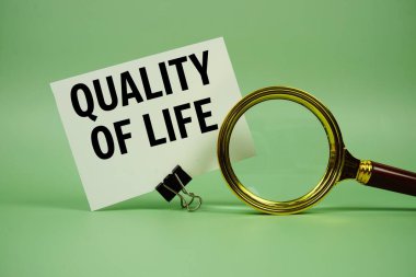 Kağıt üzerinde yeşil zemin üzerinde büyüteç bulunan Yaşam Kalitesi metin mesajı