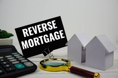 Ev modeli, hesap makinesi ve ahşap zemin üzerindeki büyüteçle İpotek mesajını tersine çevir