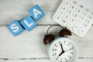 Tahta zemin üzerinde alarm saati ve hesap makinesi bulunan SLA (Servis Düzey Anlaşması) metni