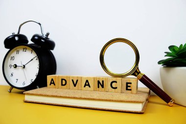 Tahta bloklar alfabe harfli büyüteç ve alarm saati sarı arkaplanda ADVANCE metin mesajı