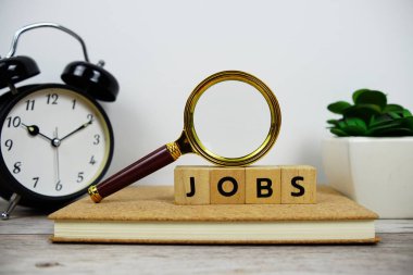 Tahta bloklar alfabe harfli büyüteç ve alarm saati. Ahşap arka planda JoBS metin mesajı.