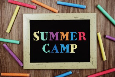 Tahtaya tebeşirle yazılmış yaz kampı metni ahşap arka planda çeşitli renkler var.