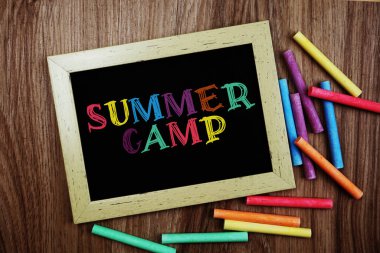 Tahtaya tebeşirle yazılmış yaz kampı metni ahşap arka planda çeşitli renkler var.