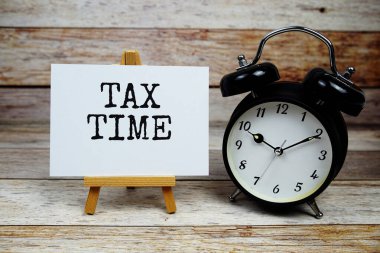 Tahta zemin üzerinde alarm saati olan kağıt üzerinde vergi zamanı metni