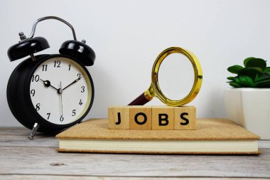 Tahta bloklar alfabe harfli büyüteç ve alarm saati. Ahşap arka planda JoBS metin mesajı.