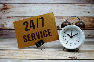 Kağıt üzerinde 7 / 24 servis metni ve ahşap zemin üzerinde alarm saati