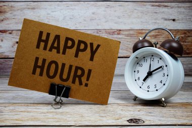 Kağıt üzerinde, ahşap zemin üzerinde alarm saati olan Happy Hour metni