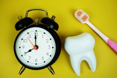 Diş fırçası ve beyaz diş fırçası modeli sarı arka planda alarm saati diş hijyeni kavramı