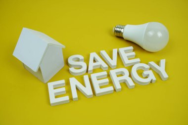 Ev modeli ve sarı zemin üzerindeki LED ampulleri, tasarruf ve çevre dostu kavramı içeren Enerji alfabesi harflerini kaydet