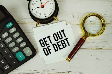 Tahta zemin üzerinde büyüteç, alarm saati ve hesap makinesi olan yapışkan notla Borçtan Çık metni yaz