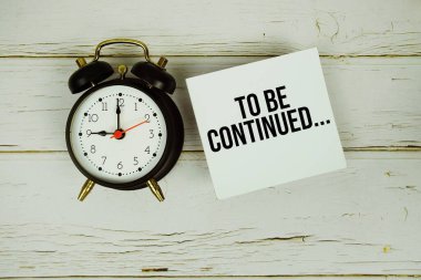 Devam Edecek... Yapışkan notta mesaj ve ahşap arka planda alarm saati