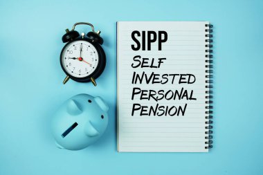 SIPP 'nin kısaltması: Not defterindeki Kişisel Yatırım Emeklilik metni ve mavi arka plandaki domuzcuk bankası ve alarm saati.