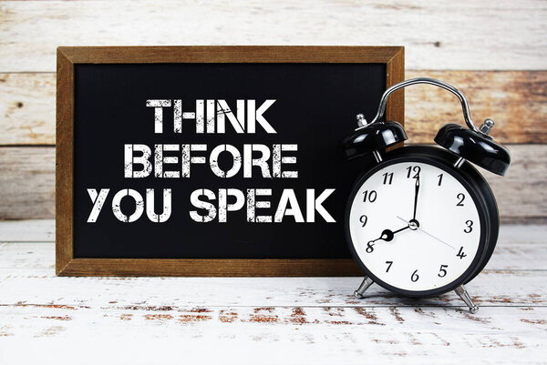 Подумайте, прежде чем говорить текстовое сообщение и будильник на деревянном фоне