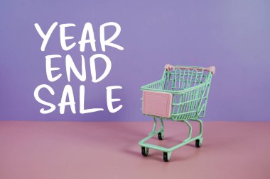 Yıl sonu satışı metni, mor ve pembe geometrik arkaplan üzerine alışveriş arabası.