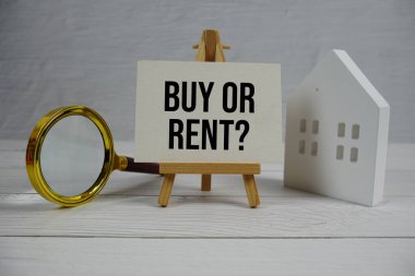 Almak mı, kiralamak mı? Beyaz Saray modeli ve ahşap arka planda büyüteçle kağıt kart üzerinde metin